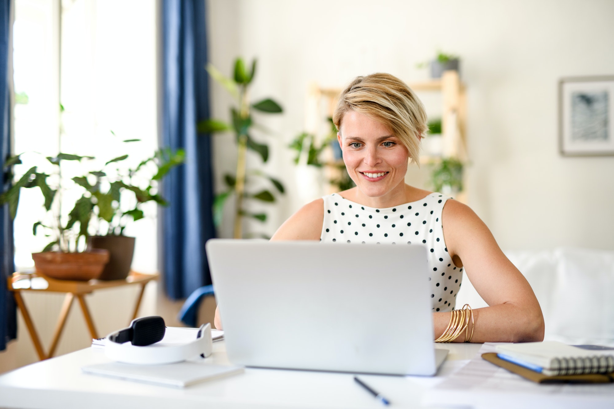 Cheerful young businesswoman with laptop indoors in home office, working