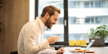 man holding teacup infront of laptop on top of table inside the room