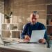 Middle aged man working in a home office and using laptop and paper documents